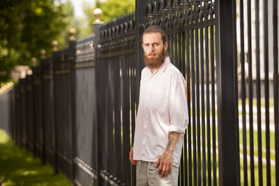 Portrait of young man standing against fence