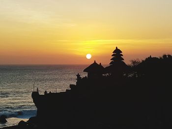 Silhouette building by sea against sky during sunset