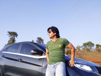 Young man looking away against clear blue sky with car posing