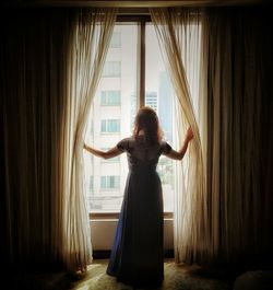 Rear view of woman standing against window at home