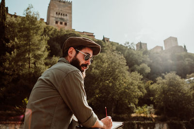 Man writing in book while standing outdoors