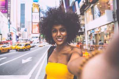 Portrait of happy young woman with afro hairstyle taking selfie on city street