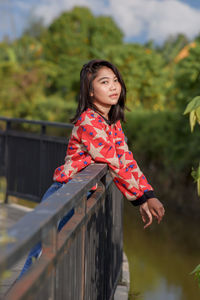 Portrait of young woman standing by railing