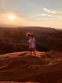 Woman tossing hair while standing on rock formation against sky during sunset