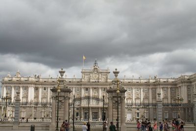 Tourists in front of building against cloudy sky