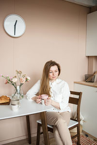 Tired woman with disheveled hair and a lowered look sits in kitchen.