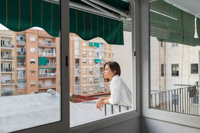 Side view of young lady in casual white shirt on balcony in sunny morning