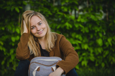 Portrait of smiling young woman with blond hair sitting against plants