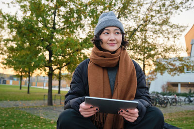 Portrait of young woman using mobile phone while sitting on field