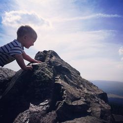 Side view of boy standing on rock against sky
