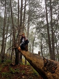 Young man standing by tree trunk in forest