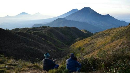 Rear view of people looking at mountains against sky