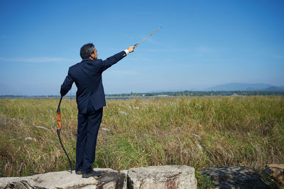 Businessman with bow and arrow on field against sky