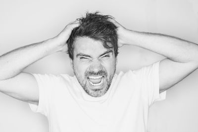 Close-up portrait of frustrated man with hands in hair against white background