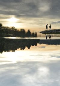 Silhouette people on lake against sky during sunset