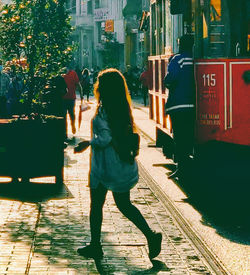 Full length rear view of woman walking on footpath in city