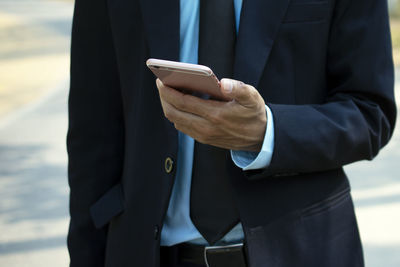 Midsection of businessman using mobile phone while standing outdoors