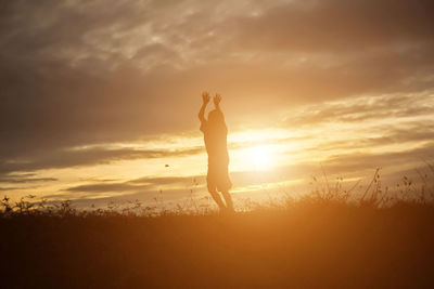 Silhouette woman standing on field against sky during sunset