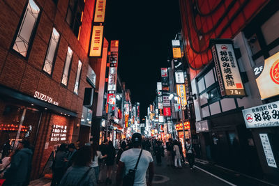 People walking on illuminated street amidst buildings at night