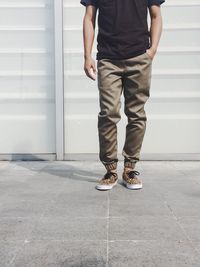 Low section of man standing on footpath against wall