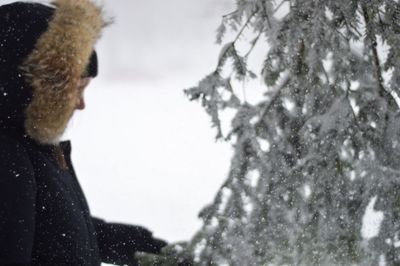 Woman standing by snow covered tree during winter