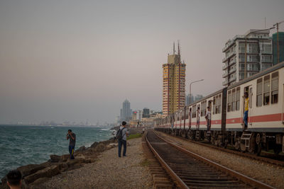 People on railroad tracks in city against clear sky