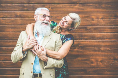 Smiling woman embracing senior man while standing against wooden door