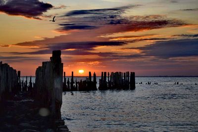 Silhouette wooden posts on beach against sky during sunset