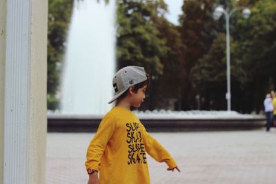 Side view of boy pointing while standing on footpath