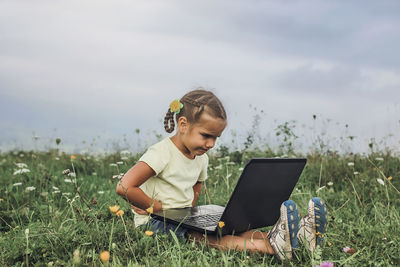 Cute girl looking at laptop while sitting on grass