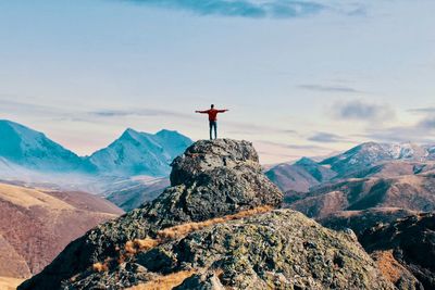 Rear view of man with arms outstretched standing against mountain on rock