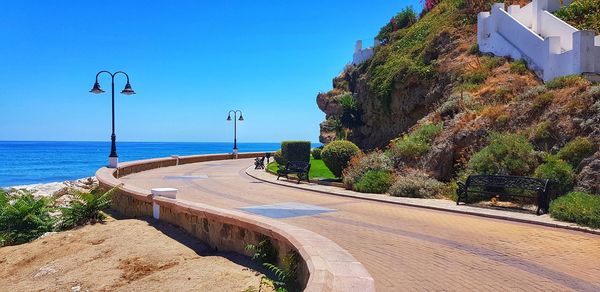 Road by sea against clear blue sky