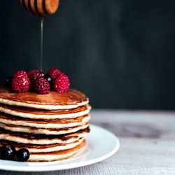 Juicy pancakes with berries and honey on a white plate, spoon, wooden table. high quality photo