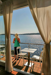 Rear view of woman near table by sea, looking away 