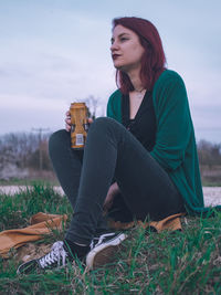 Beautiful young woman sitting on field against sky