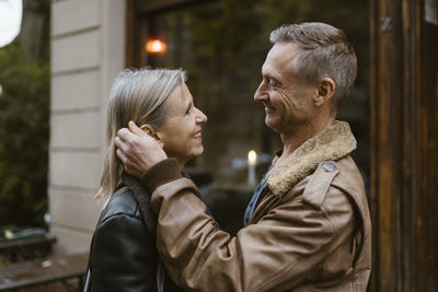 Side view of smiling man stroking woman while standing in front of restaurant