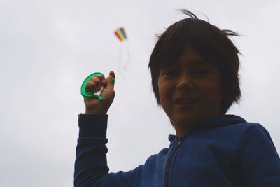Low angle portrait of boy flying kite in sky