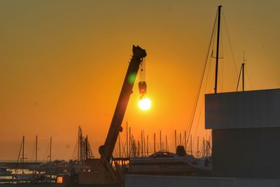 Sailboats in harbor against orange sky