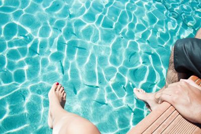 Low section of couple sitting on poolside