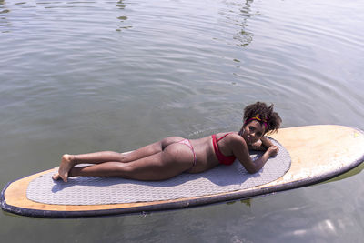 High angle view of young woman lying down on surfboard in water