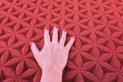 Cropped hand of woman touching patterned red wall