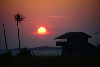 Silhouette house by sea against orange sky