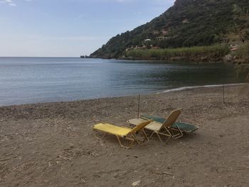 Empty chairs on beach against sky