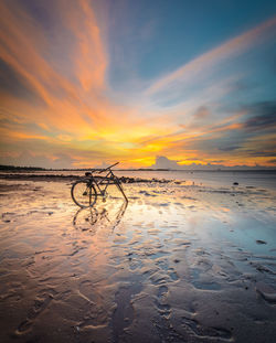 Bicycle at frozen beach against sky during sunset
