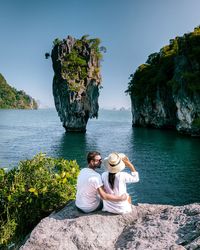 People sitting on rock by sea against sky