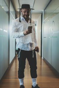 Man wearing hat using mobile phone while standing in corridor