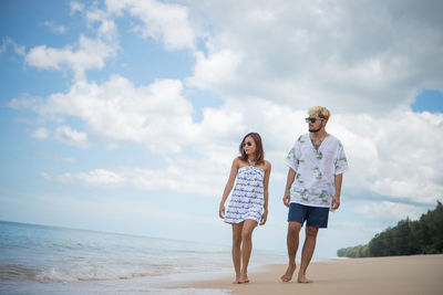 Man and woman walking at beach against sky