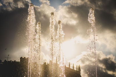 Firework display over fountain in city against sky