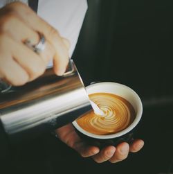 Close-up of hand pouring cream in coffee cup