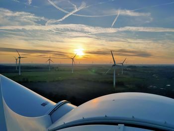 Wind turbines on field against sky during sunset